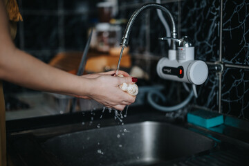 Hands thoroughly washing a mushroom in a kitchen sink. The background features a modern faucet and water flowing, demonstrating hygiene and food preparation practices in a domestic setting.