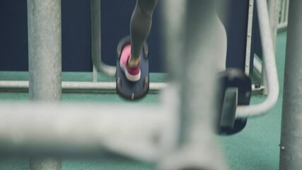 Fragment of a woman’s body in gray leggings exercising at an outdoor fitness machine, focus on legs and sportswear