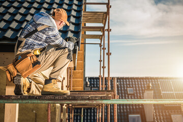 Construction Worker Inspecting Tools While Kneeling on Scaffolding at a Building Site During Sunset
