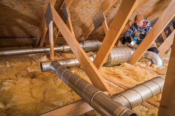 Attic Worker Repairing Ventilation System in a Residential Building During Winter Season
