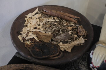 A rustic wooden bowl filled with traditional dried herbal medicine ingredients, including cinnamon sticks, shredded bark, dried leaves, and botanicals