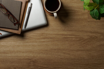 Overhead view of wooden desk with notebook, laptop, pen, eyeglasses, coffee, and copy space on the right.