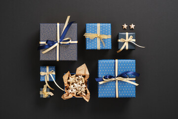 A composition of neatly arranged gifts of different sizes in blue paper and with gold ribbons on a black background.