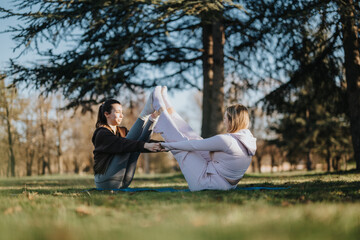Two women exercising together, engaging in partner yoga poses in an open park, highlighting teamwork and outdoor recreational practices for maintaining health and fitness.