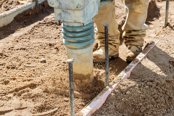 Rammer compacts soil as construction worker prepares ground at building site under work day