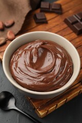 Tasty pudding in bowl, pieces of chocolate and cocoa beans on black table, closeup