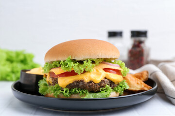 Tasty cheeseburger with sauce and potato wedges on white table, closeup