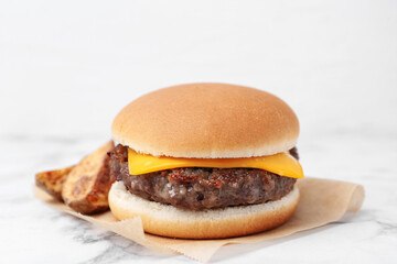 Tasty cheeseburger with potato wedges on white marble table, closeup