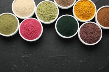 Different superfood powders in bowls on dark textured table, flat lay. Space for text