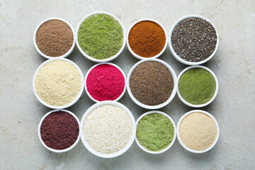Different superfood powders in bowls on grey textured table, flat lay