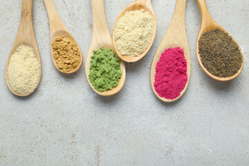 Different superfood powders in spoons on grey textured table, flat lay. Space for text
