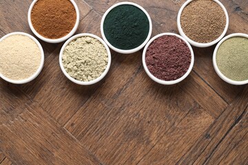 Different superfood powders in bowls on wooden table, flat lay. Space for text