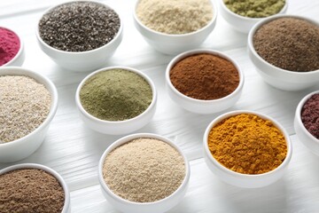 Different superfood powders in bowls on white wooden table, above view