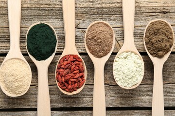 Different superfoods in spoons on wooden table, flat lay