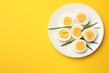 Boiled eggs and green onions on yellow background, top view. Space for text