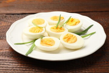 Halves of hard boiled eggs with green onions on wooden table, closeup