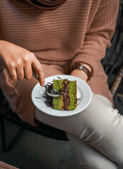 A slice of cake with a layer of cream and chocolate sprinkles on a wooden table, enjoyed by a woman. The atmosphere of a cozy cafe