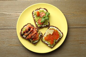 Different delicious avocado sandwiches on wooden table, top view