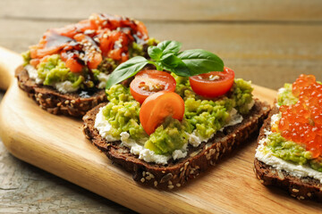 Different delicious avocado sandwiches on wooden table, closeup