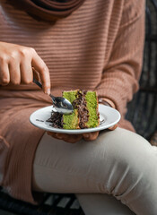 A slice of cake with a layer of cream and chocolate sprinkles on a wooden table, enjoyed by a woman. The atmosphere of a cozy cafe