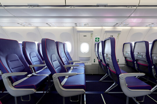 Empty interior of new modern airplane Airbus A321 XLR with blue seats and no passangers. Photographed in ambiental light. Selective focus..