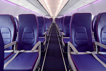 Empty interior of new modern airplane Airbus A321 XLR with blue seats and no passangers. Photographed in ambiental light. Selective focus..