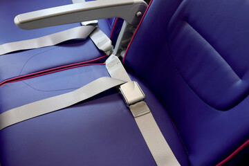 Close up of seat belt of empty chair and interior of new modern airplane Airbus A321 XLR with blue seats and no passangers. Photographed in ambiental light. Selective focus.