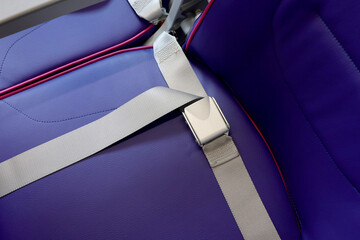 Close up of seat belt of empty chair and interior of new modern airplane Airbus A321 XLR with blue seats and no passangers. Photographed in ambiental light. Selective focus.