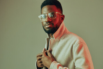 Stylish young man in a beige coat with glasses, exuding confidence against a soft pastel background, suitable for fashion and lifestyle content
