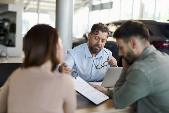 Car salesman explaining the contracts to a couple during a meeting at a car dealership.