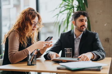 Two people, one using a smart phone, collaborate in rustic co working cafe environment, engaging in a discussion to work on their creative projects or tasks. Ideas flow in a casual but refined