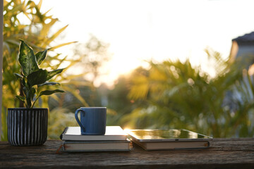 Blue cup, notebook, and potted plant on a rustic wooden balcony table outdoors