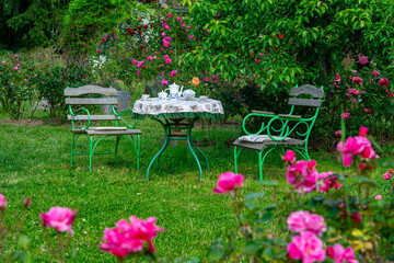 Serenic image of a charming garden with a table set for tea amidst blooming roses and greenery, evoking calmness and leisure