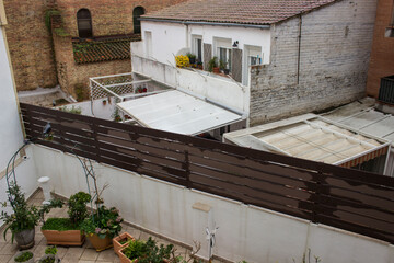 view from above, onto a large balcony with various green flowerpots, and onto another house