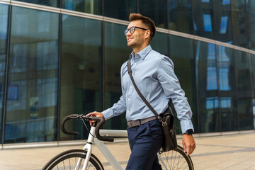 Walking confidently with a bicycle near modern architecture on a sunny day in the city
