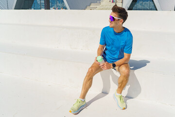 Energetic athlete taking a break in the sun while hydrating at a modern sports venue