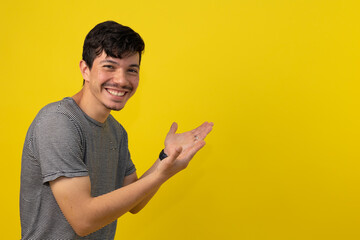 Smiling young freckled man in a striped shirt pointing at a space for text on a yellow background,...