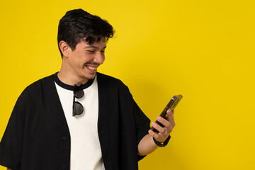 Young freckled man with a mustache smiling while looking at his cell phone on a yellow background...