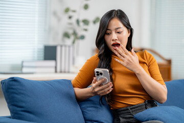 Shocked young woman is using mobile phone at home, surprised female reading news, unbelievable notification on smartphone