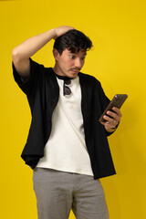 Vertical image of a young freckled man with a mustache smiling with a surprised expression while looking at his cell phone on a yellow background with space for advertising