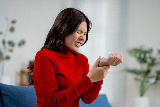 Asian woman holding her painful wrist, suffering from wrist pain, arthritis, carpal tunnel syndrome