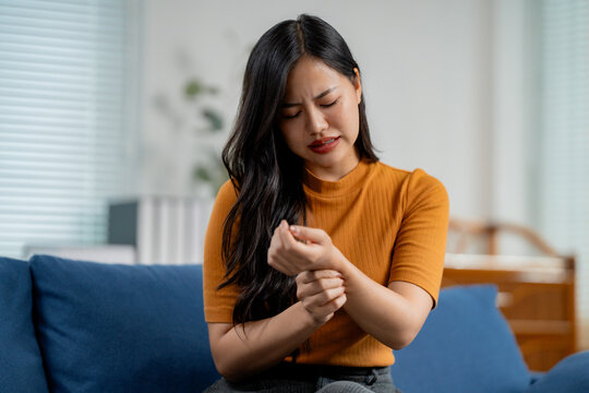 Asian woman massaging her painful wrist at home, suffering from arthritis, carpal tunnel syndrome or other joint disease