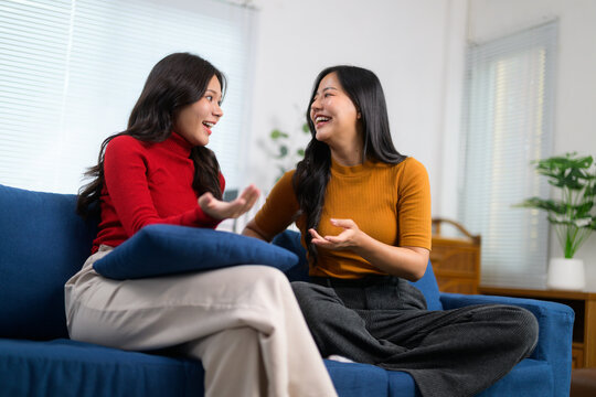 Two friends are sharing a lighthearted moment, engaging in conversation and laughter while relaxing on a sofa in a cozy living room