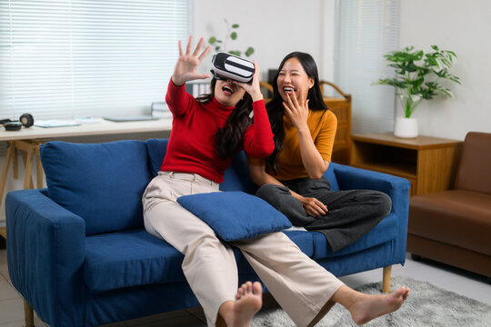 Two female friends experiencing virtual reality at home using a headset, having fun and laughing