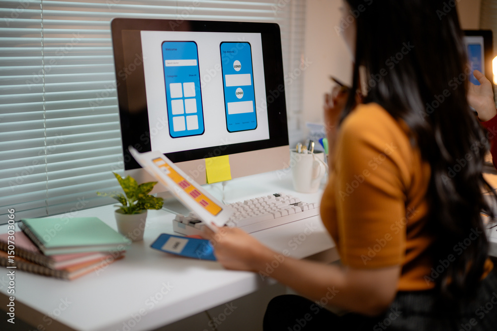 Fototapete female web designer working at desk comparing mobile app design on computer and paper prototype