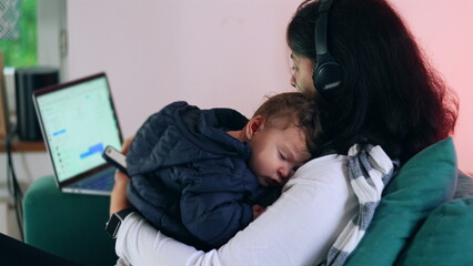 Mother holding a sleeping baby in arms while checking phone and working on laptop, blending caregiving and remote work, multitasking in home environment