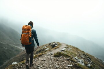 Hiker with orange backpack walks a misty rocky mountain trail