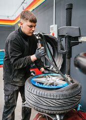 Young mechanic working on tire mounting with professional machine in an auto workshop