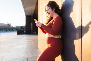 Body positive curvy woman wearing red sportswear using smartphone after fitness workout