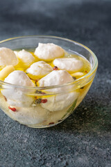 Glass bowl of labneh balls in oil, spiced with garlic and rosemary